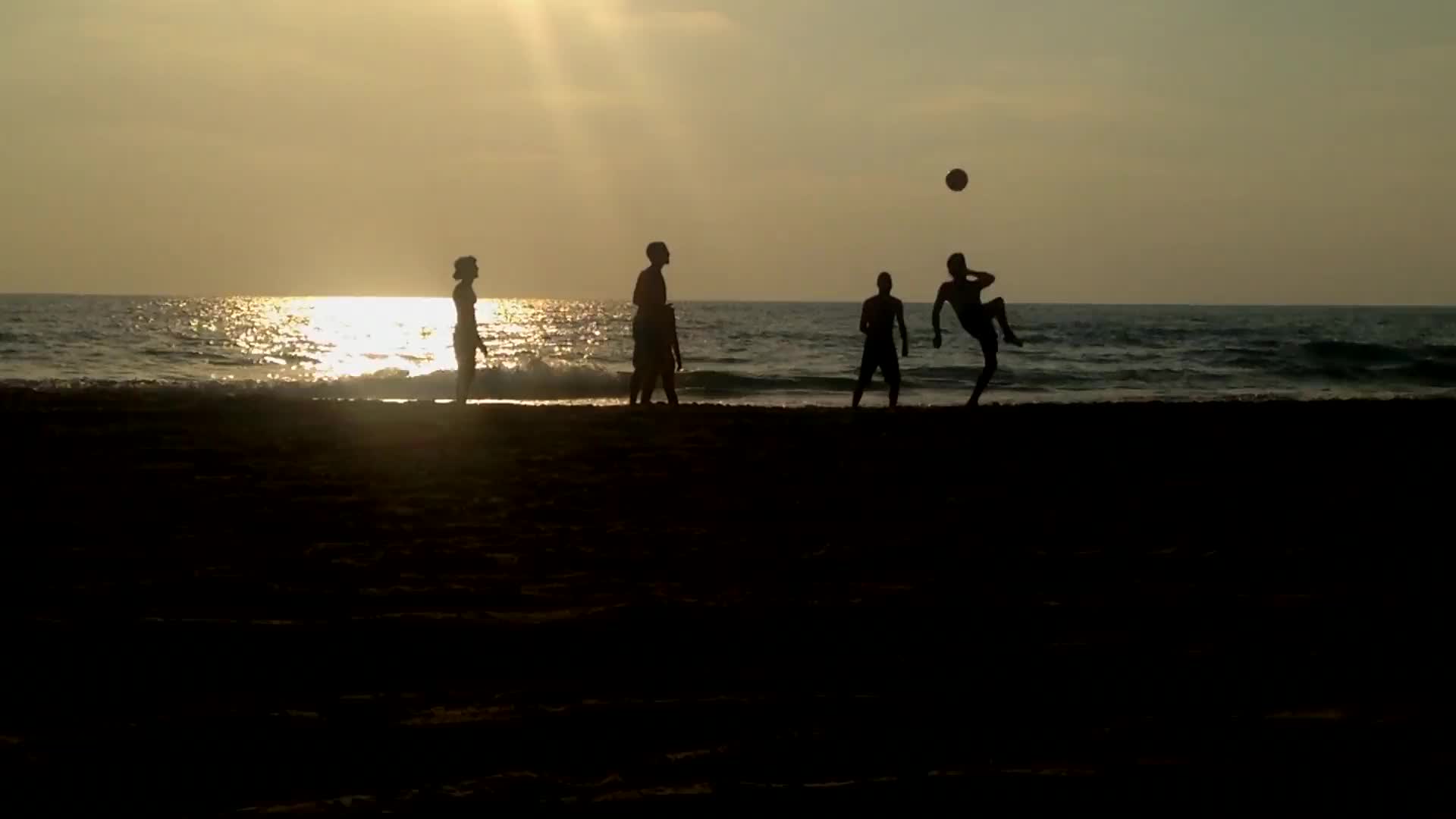 Personen die am Strand Fussball spielen.